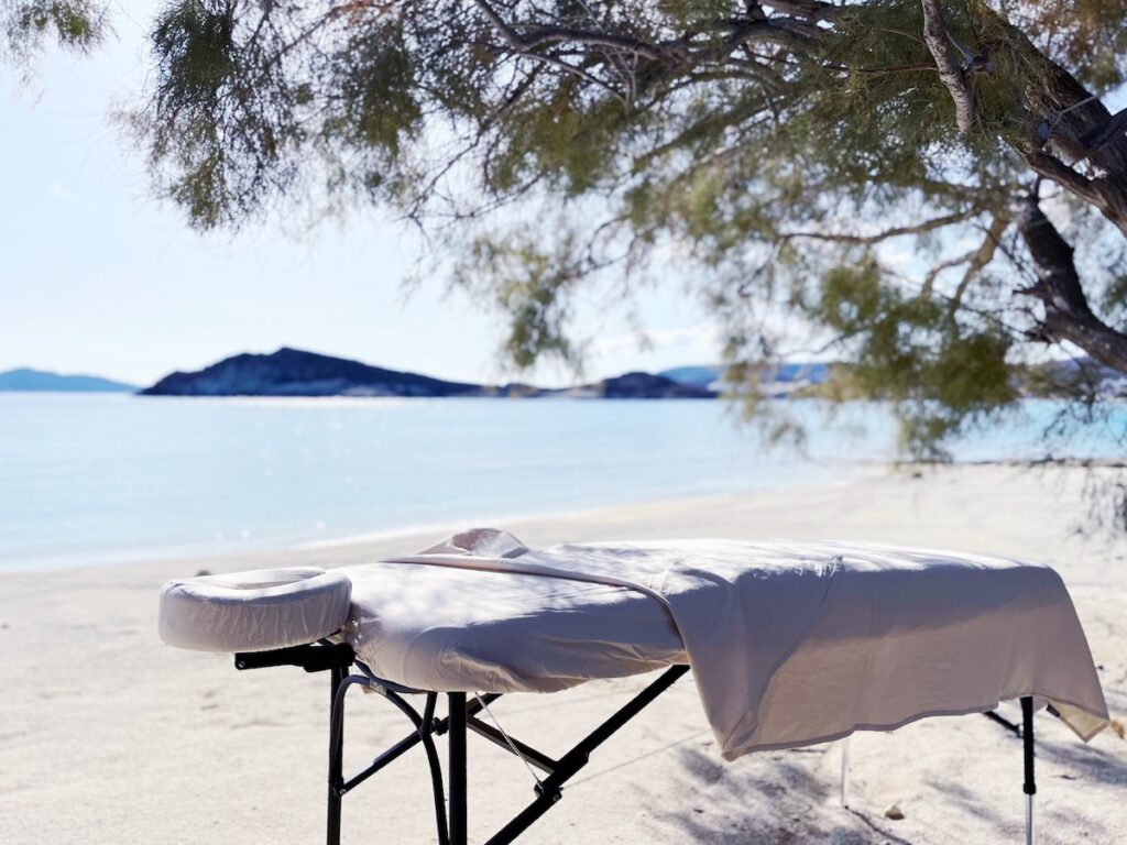 Massage table under a tree on a quiet beach on Kimolos, overlooking the Aegean Sea