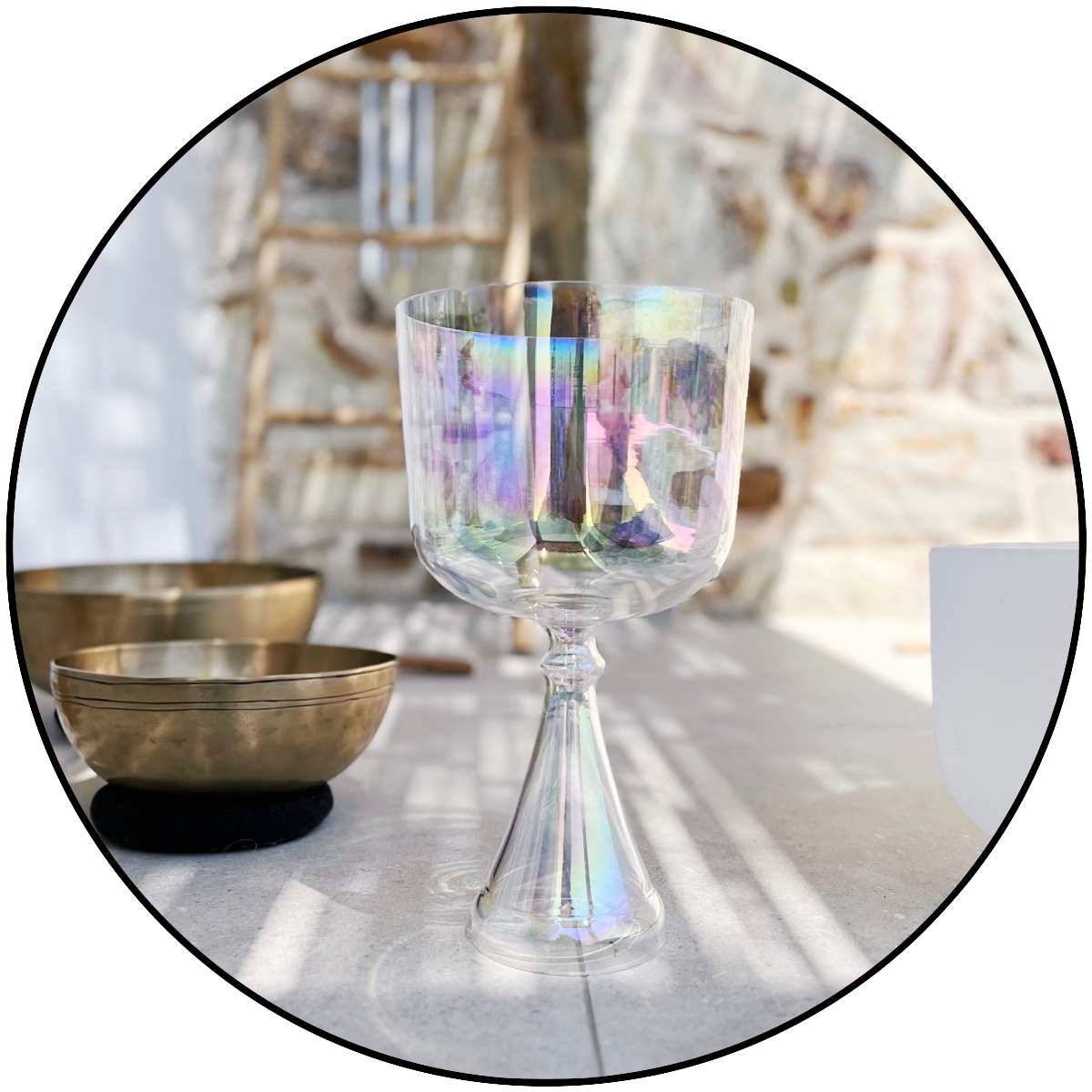 A beautiful iridescent crystal singing bowl, prominently displayed in a serene, sunlit outdoor setting, with brass Tibetan bowls in the blurred background, evoking a sense of calm and spiritual healing on Kimolos.