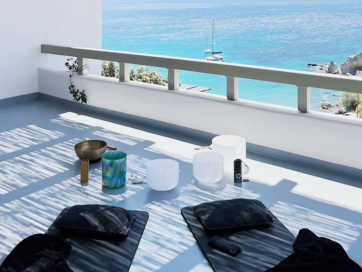 Balcony sound bath setup with crystal bowls and view of the turquoise sea on Kimolos island.