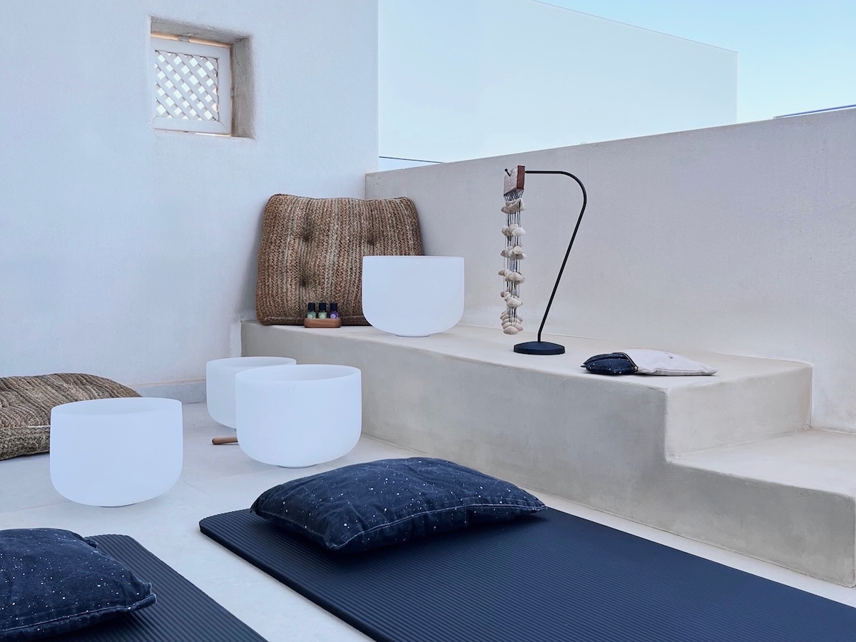 Minimalist rooftop sound bath setup with white crystal singing bowls, essential oils and shell chimes on Kimolos island.
