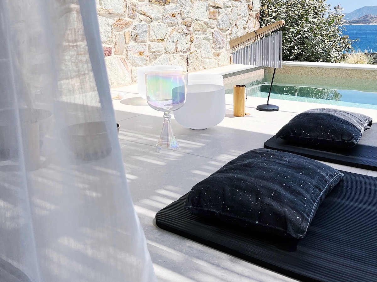 Crystal singing bowls and chimes set up for a private sound bath on a stone terrace by the pool with sea view on Kimolos island.
