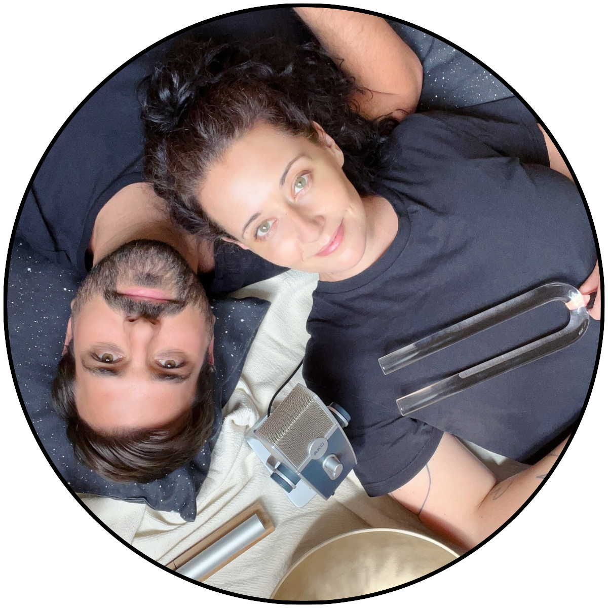 Jenny and Matthias lying on a sound healing setup with tuning fork and microphones, ready for a private sound bath session on Kimolos