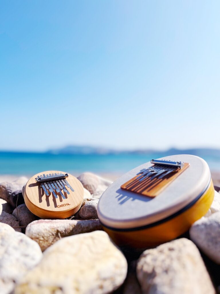 Zwei kleine Klanginstrumente – eine Kalimba und eine Sansula – auf Steinen am Strand von Kimolos, Griechenland. Ideal für achtsame Klangarbeit