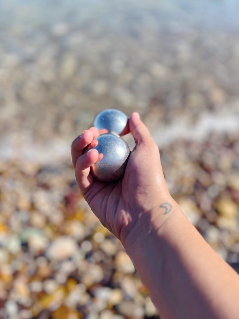 Silver Baoding Sound Balls held in hand, with sea background, for planetary-aligned Sound Healing