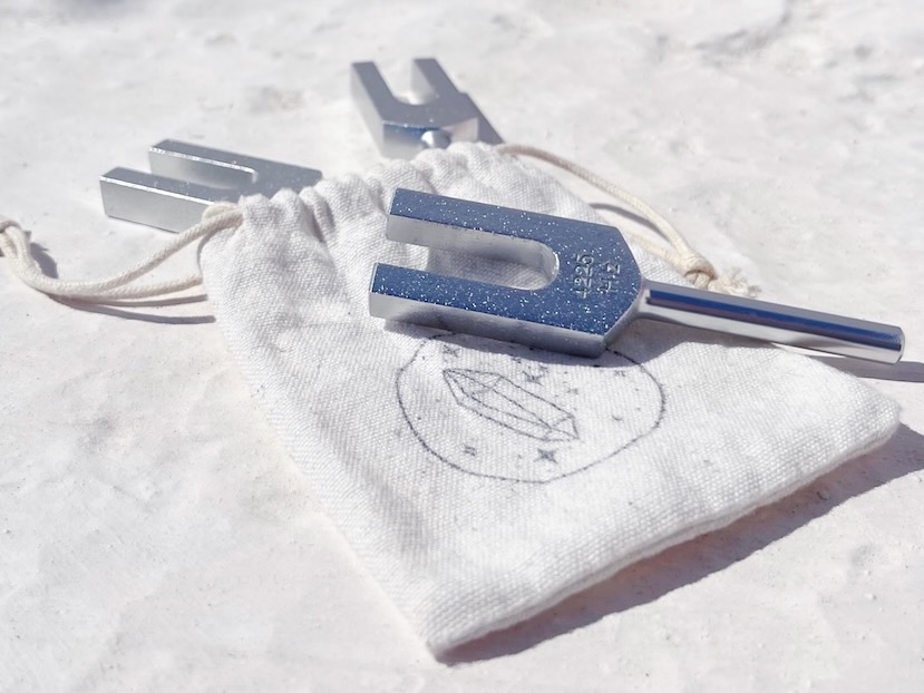 Close-up of three silver tuning forks resting on a small, white fabric bag, often used in Personalized Sound Baths with Pisces Placements or strong Neptune position.