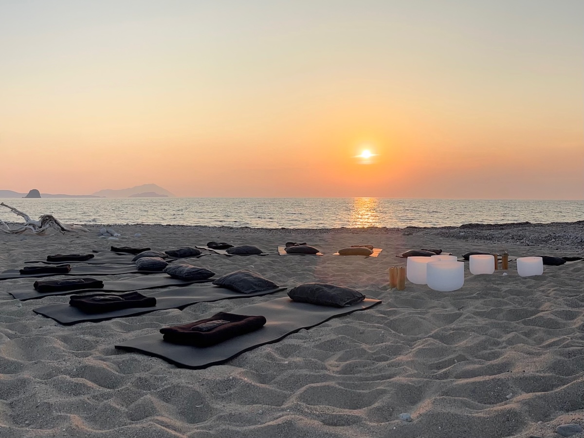 Sunset Sound Bath class on Kimolos beach with 12 mats and crystal singing bowls arranged on the sand