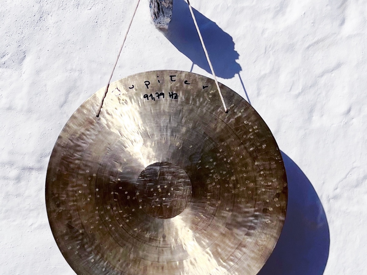 Large, golden Jupiter gong labeled “Jupiter 91.79 Hz” hangs in front of a white wall. A typical instrument for a Personalized Sound Bath for charts with Sagittarius placements.