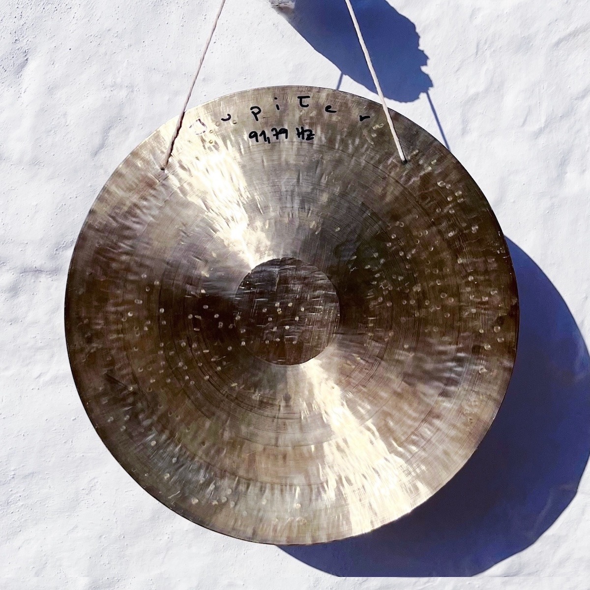 Large golden Jupiter gong in front of a white washed stone wall, used for Sound Healing in Greece