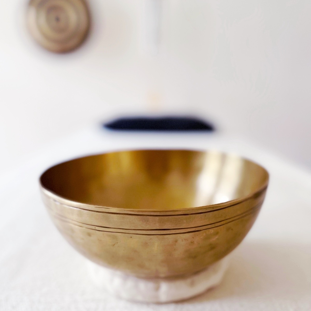 goldene Klangschale auf einer Massageliege, im Hintergrund an der Wand ein Gong