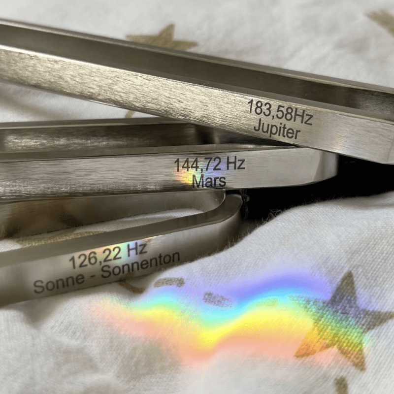 Three planetary tuning forks placed on soft fabric with rainbow light.