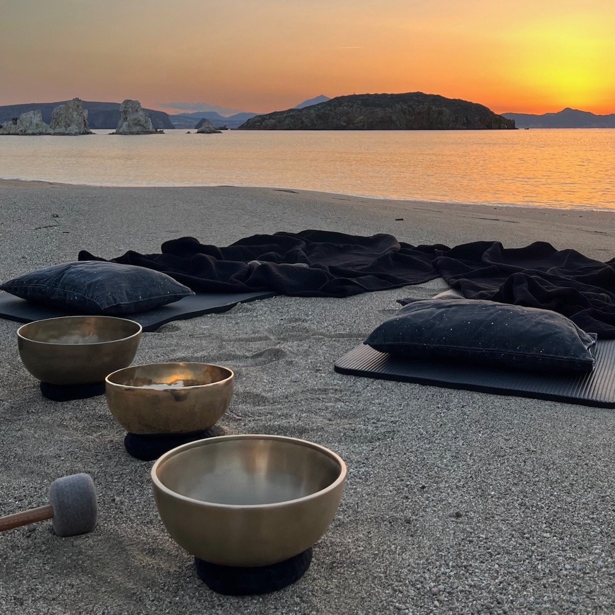 Tibetan singing bowls and mats on a beach, prepared for a couple Sound Bath at sunset on Kimolos Island in Greece