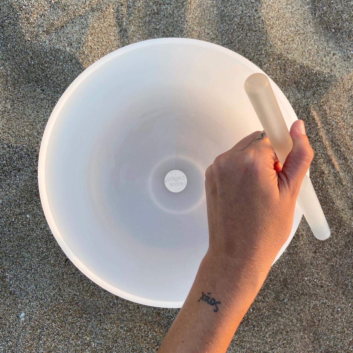 Hand playing a crystal singing bowl on the beach during a Sound Bath on Kimolos Island in Greece