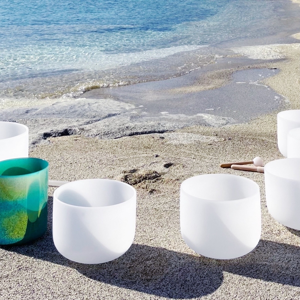 Crystal singing bowls on the beach by the Aegean Sea during an outdoor Sound Bath on Kimolos Island in Greece