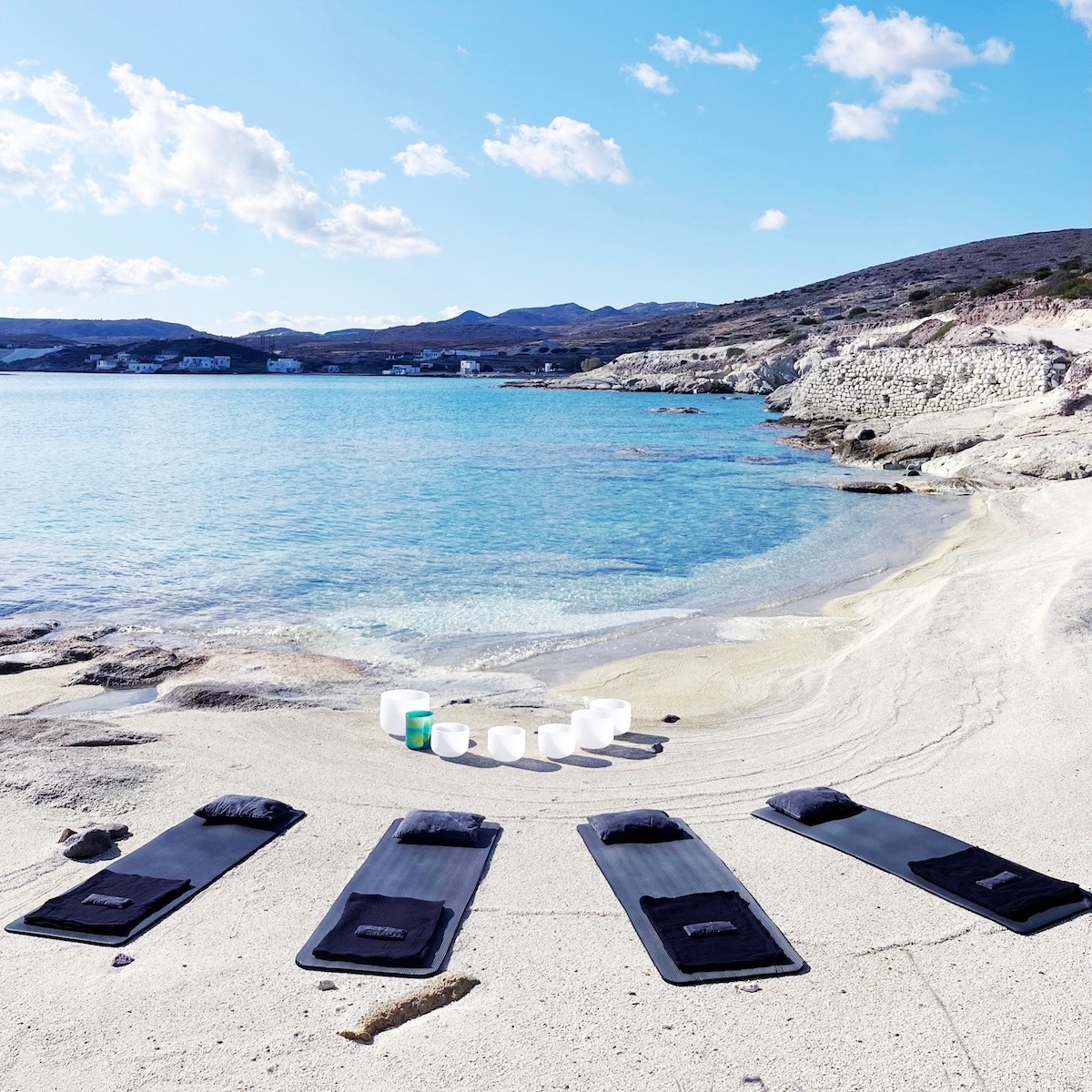 Four yoga mats with pillows and crystal singing bowls set up for a Sound Bath on a beach on Kimolos, Greece