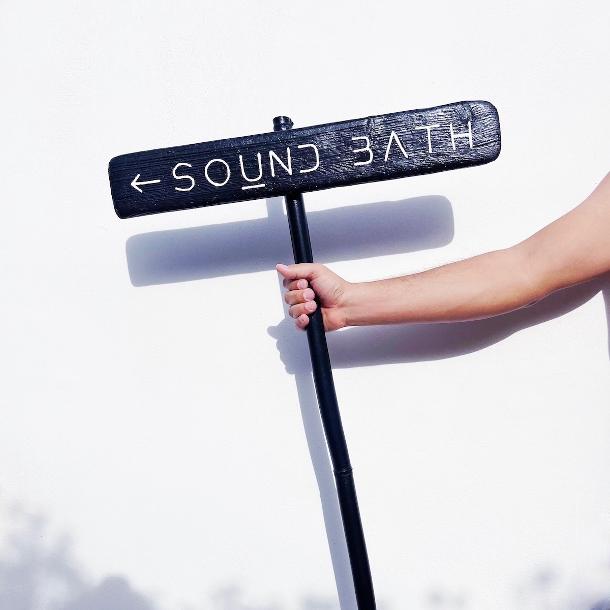 Hand holding a black Sound Bath sign in front of a white wall on Kimolos Island in Greece