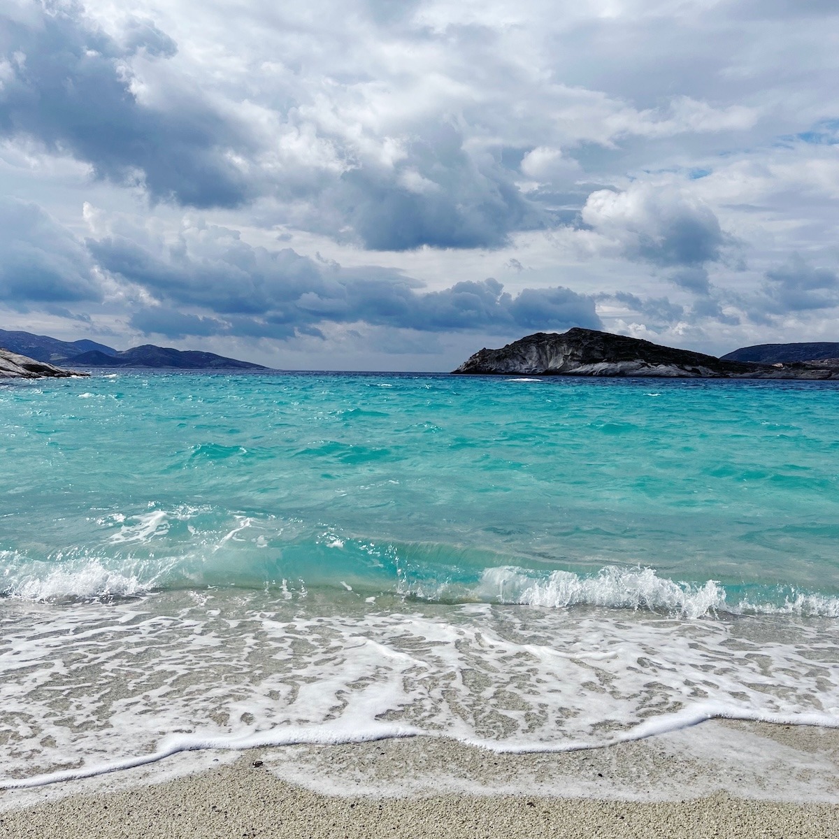 Stormy turquoise sea on Kimolos Island in Greece with waves, dramatic clouds and changing weather in the Aegean Sea